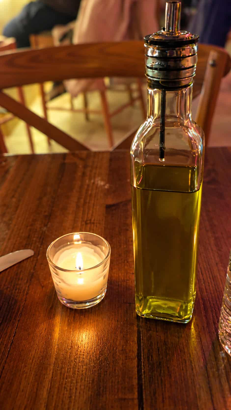 Glass bottle of olive oil sitting next to a glowing votive candle on a rustic wooden table at Ambrosia Garden