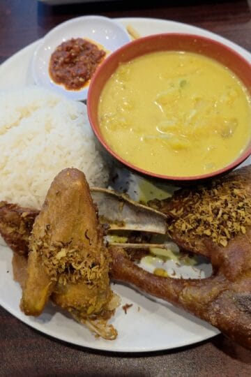 Ayam Goreng Kremes platter featuring crispy fried chicken topped with savory crumbs, steamed rice, vegetable soup, and red sambal