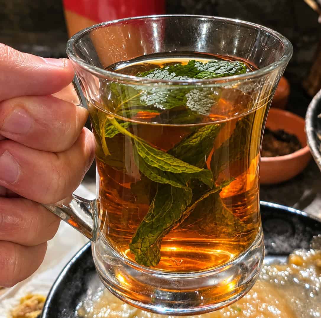 Hand holding a glass mug of hot Arabic mint tea packed with fresh green mint leaves