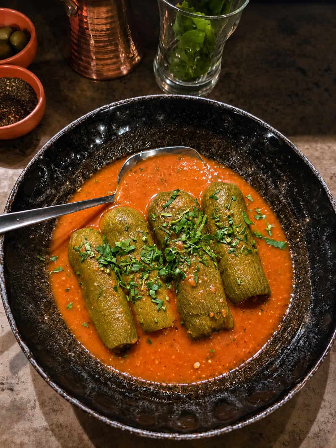 Stuffed squash kousa mahshi in a savory tomato sauce topped with chopped herbs in a ceramic bowl