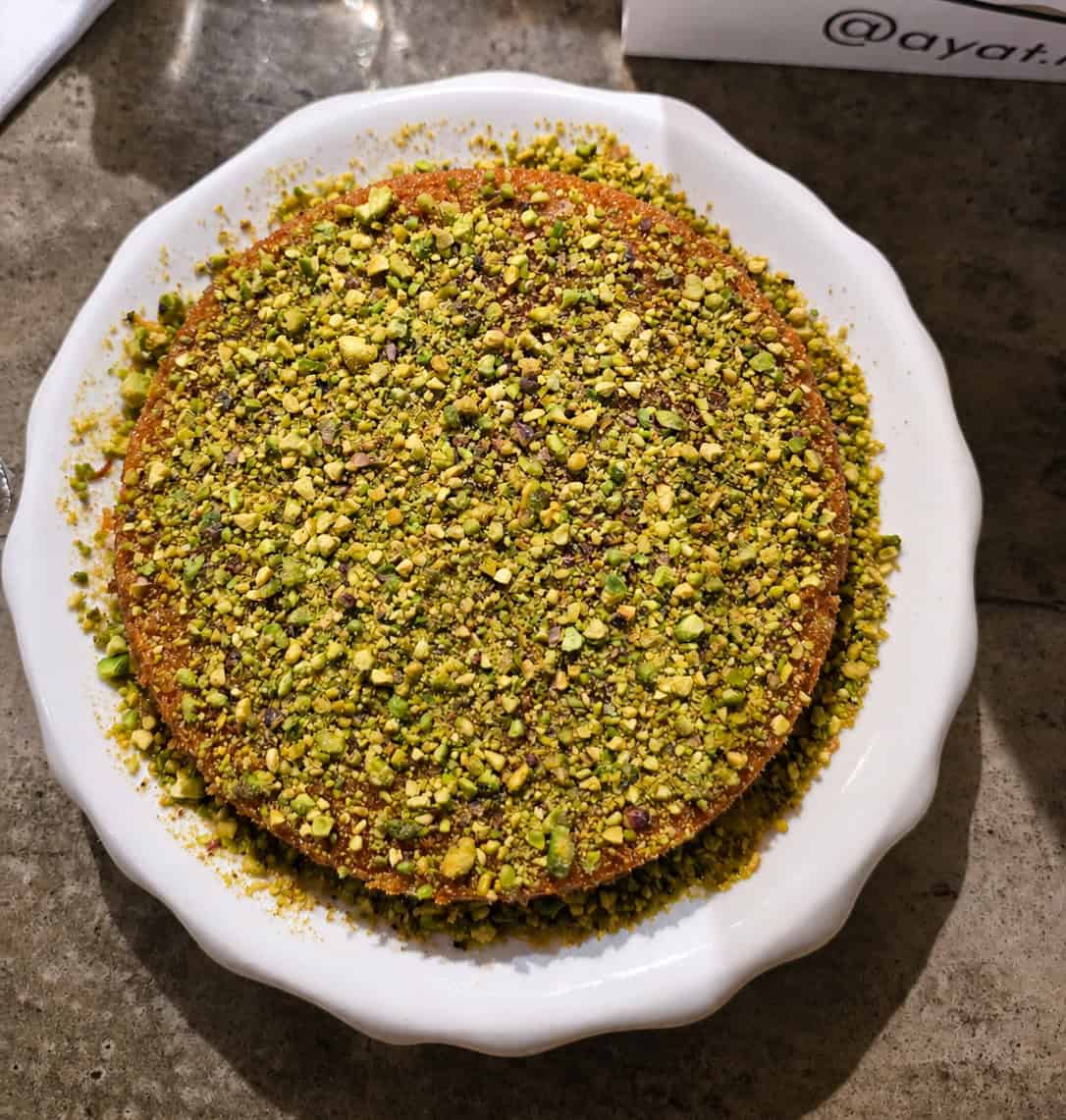 Top-down view of a round Palestinian Kunafa dessert completely covered in crushed green pistachios