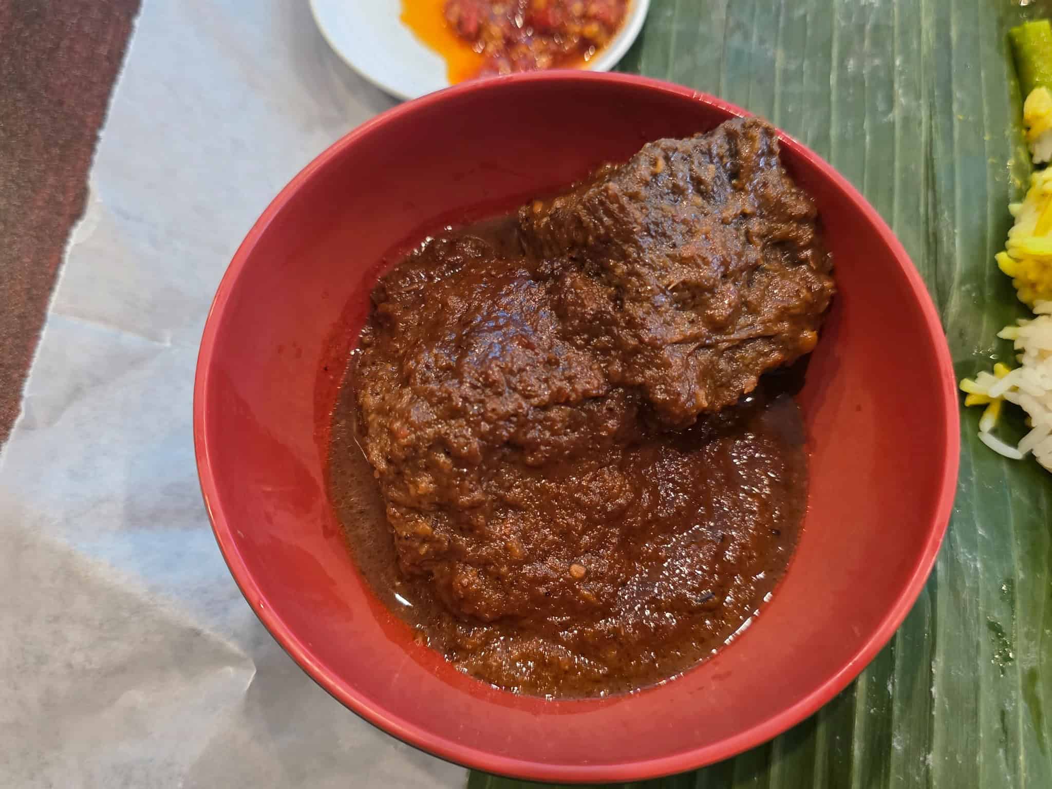 Red bowl of tender Indonesian Beef Rendang simmered in rich coconut milk and aromatic spices