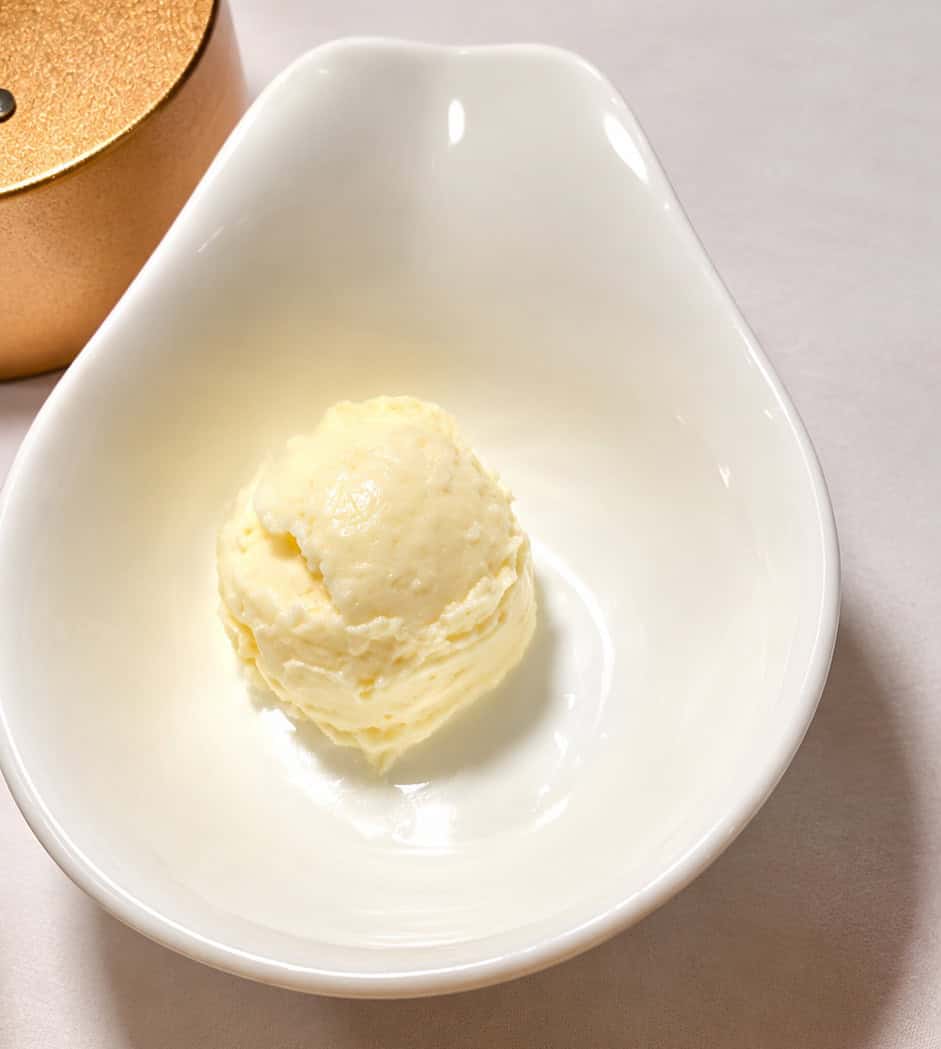 A scoop of creamy butter in a white teardrop dish served with warm Turkish bread