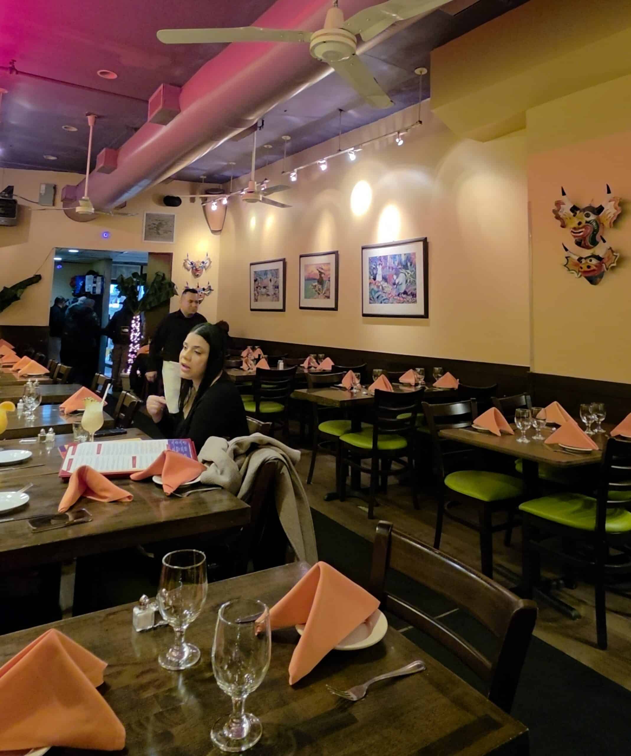 Casual Latin-inspired dining room interior at Cabana featuring yellow walls, framed art, decorative masks, and dark wooden tables