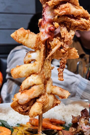 Close-up view of Calamares Gigantes featuring a massive deep-fried whole squid served upright on a wooden skewer