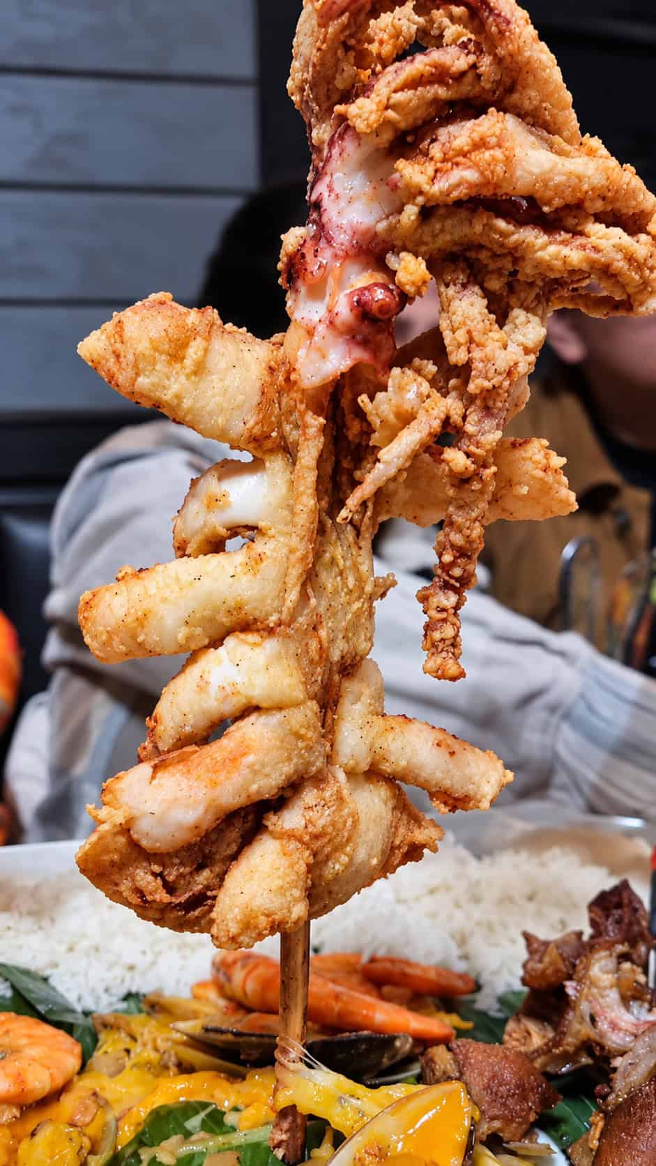 Close-up view of Calamares Gigantes featuring a massive deep-fried whole squid served upright on a wooden skewer