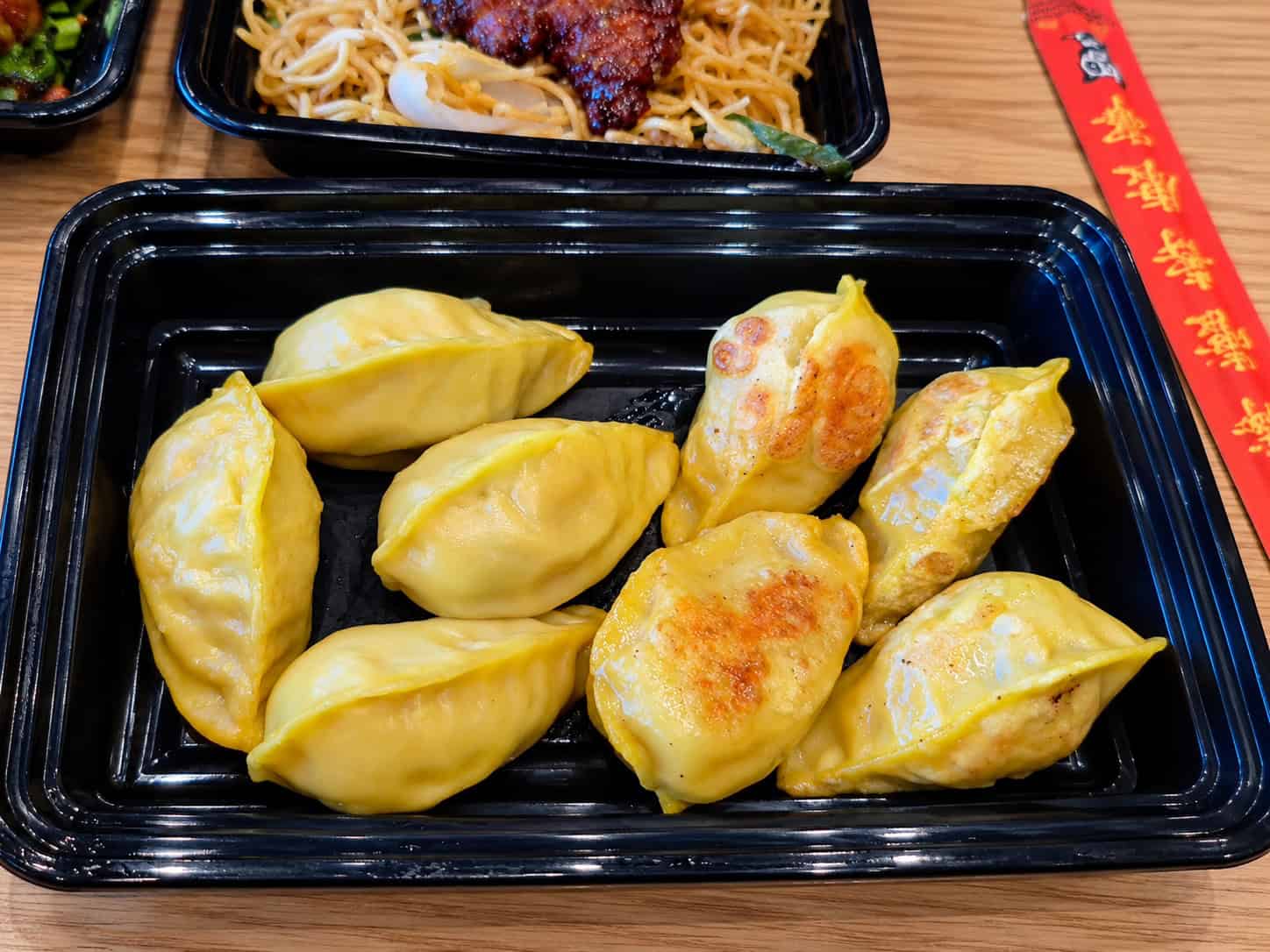Rectangular black tray of yellow-wrapped Chicken and Cabbage Dumplings prepared half steamed and half pan-fried
