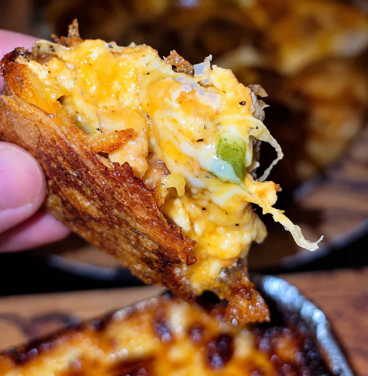 Hand holding a slice of Egyptian chicken fajita feteer showing a gooey melted cheese pull