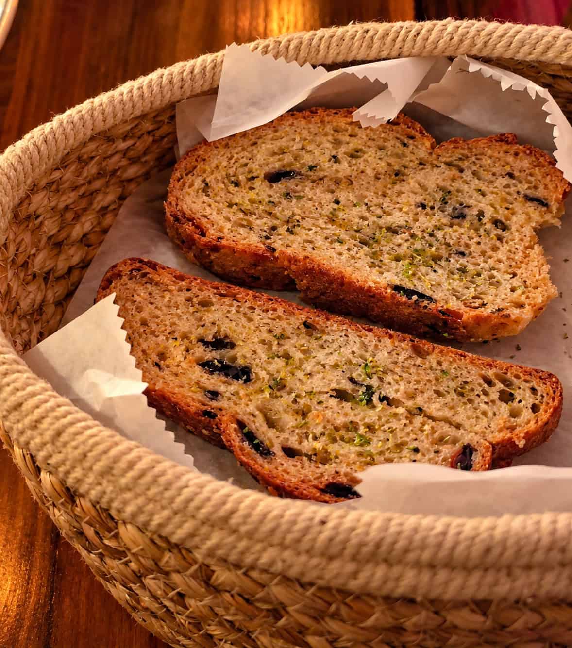 Woven basket containing warm slices of Greek artisan bread studded with herbs and black olives