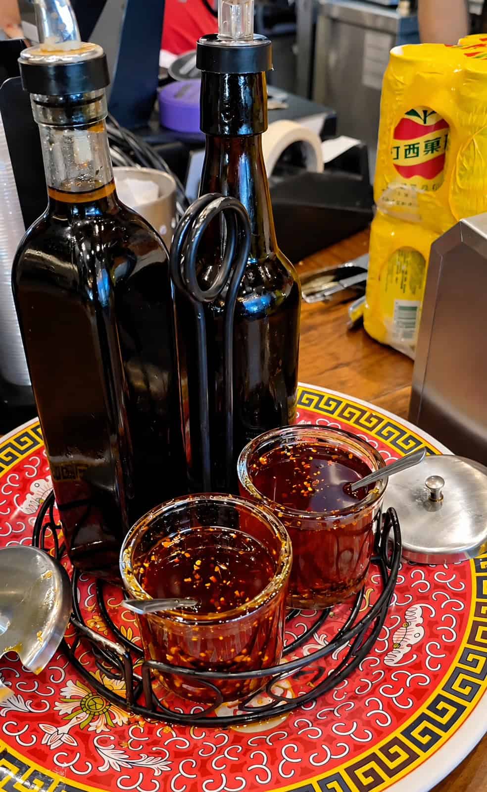 Condiment station set up with glass jars of chili oil with garlic flakes and glass bottles of soy sauce and black vinegar