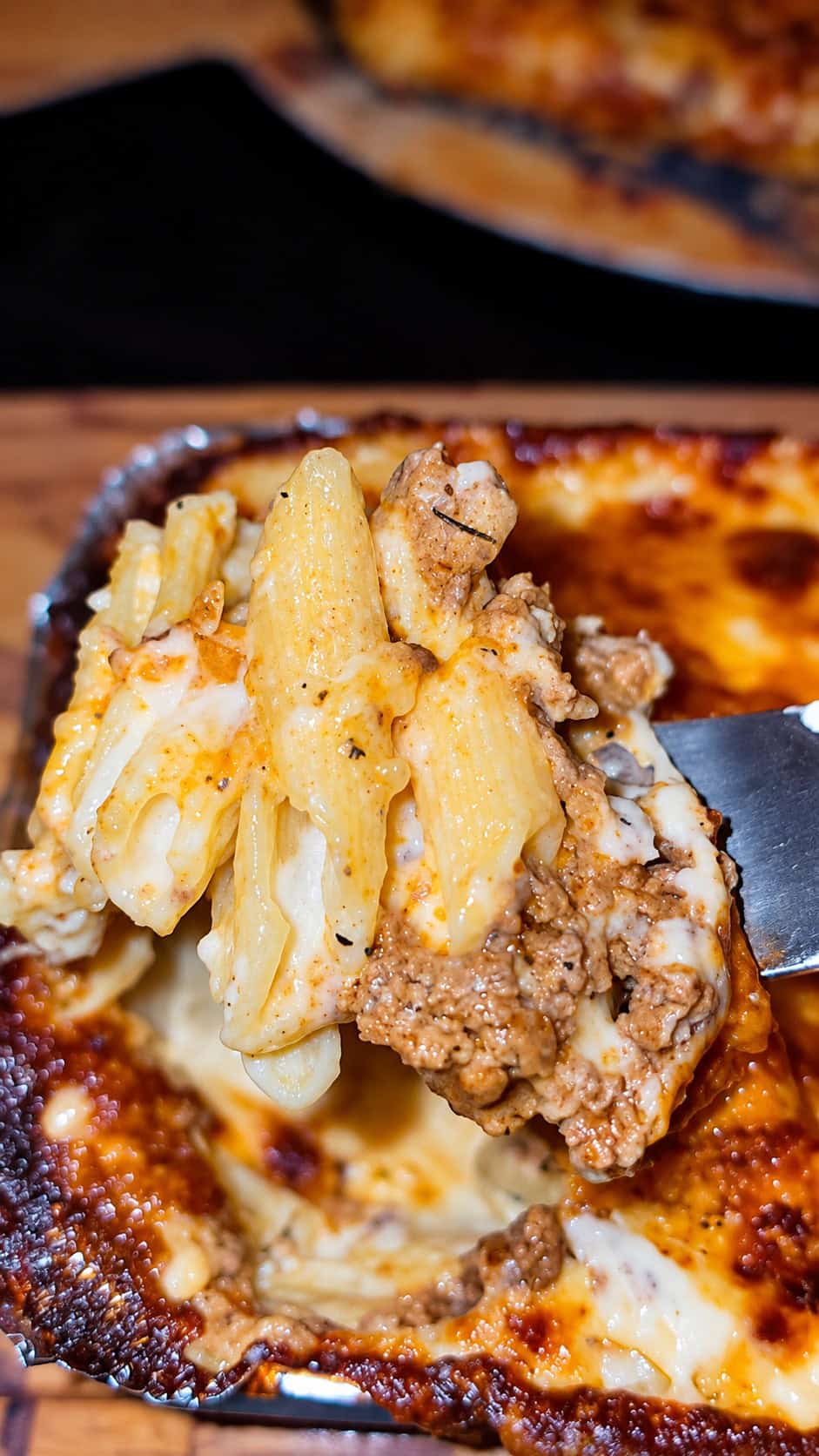 Forkful of penne pasta mixed with seasoned minced beef and creamy béchamel sauce