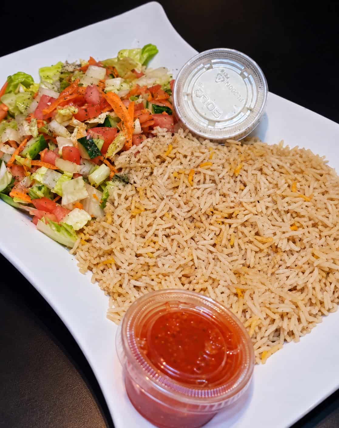 Platter of fluffy seasoned basmati rice alongside fresh diced cucumber, tomato, and lettuce salad with dipping sauces