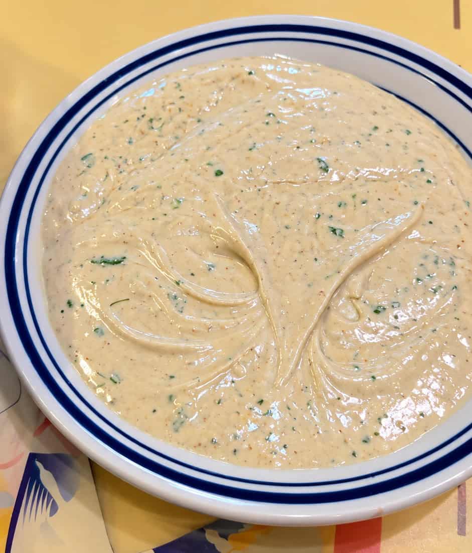 Bowl of creamy herb-flecked tahini dip with olive oil swirl