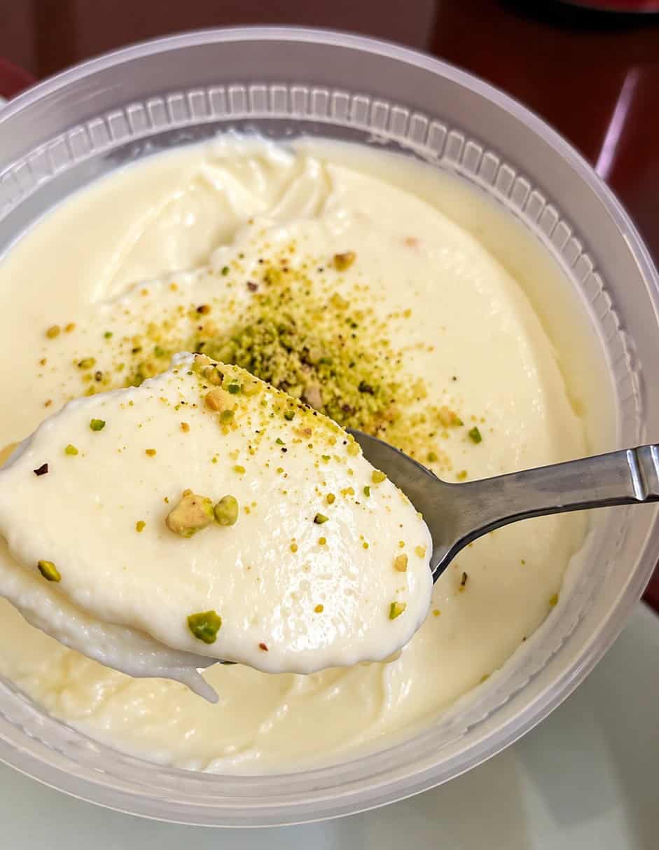 Spoonful of creamy white Firnee pudding garnished with crushed pistachios