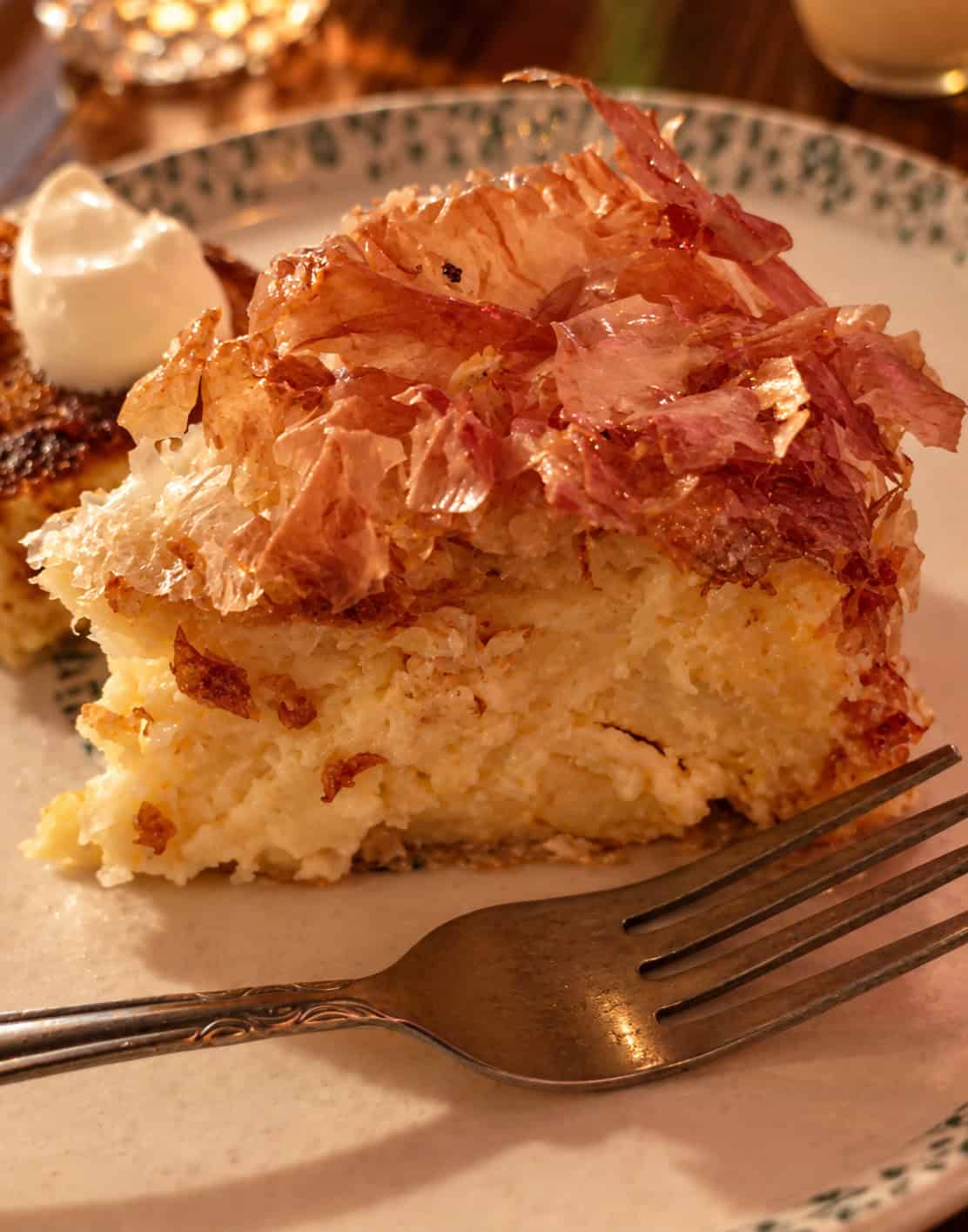 Slice of Galaktoboureko with golden crispy phyllo pastry, thick semolina custard, and a dollop of cream