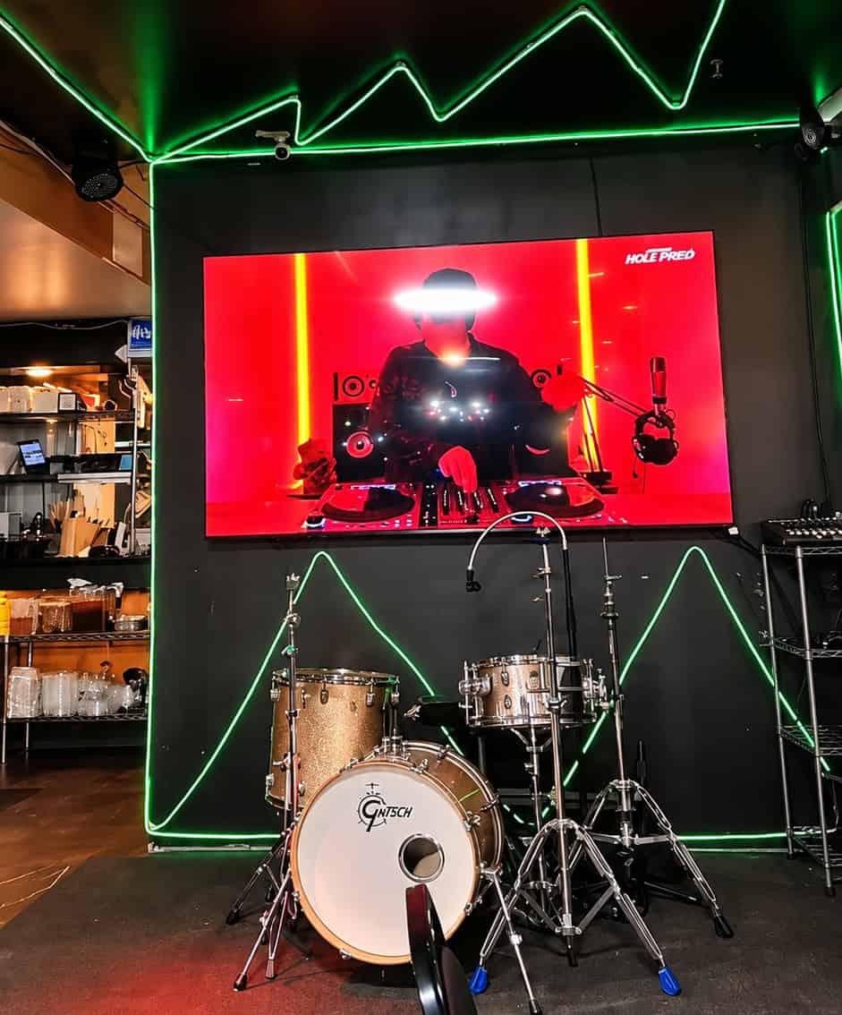 Performance stage inside Kusina Pinoy Bistro set up with drum kit, screen display, and neon green accent lights