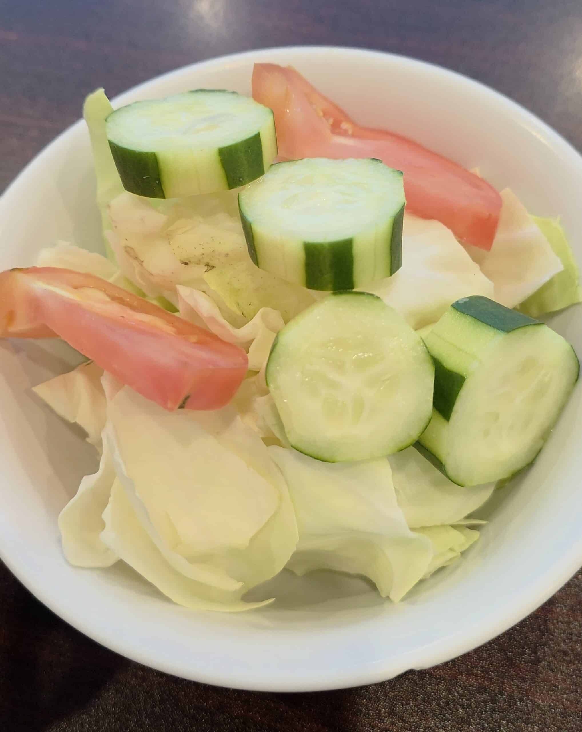 Bowl of fresh Lalapan featuring sliced cucumbers, cabbage, and tomato wedges