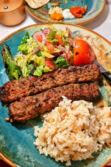 Platter of two grilled Lamb Adana Kebabs served with seasoned rice, fresh salad, and grilled pepper and tomato