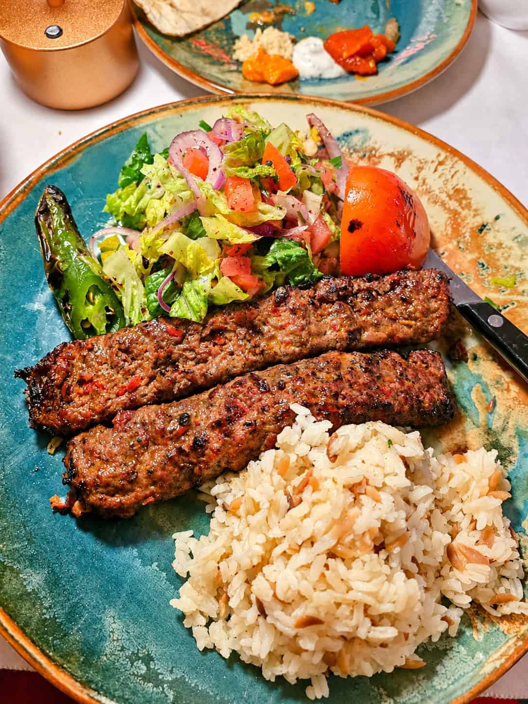 Platter of two grilled Lamb Adana Kebabs served with seasoned rice, fresh salad, and grilled pepper and tomato