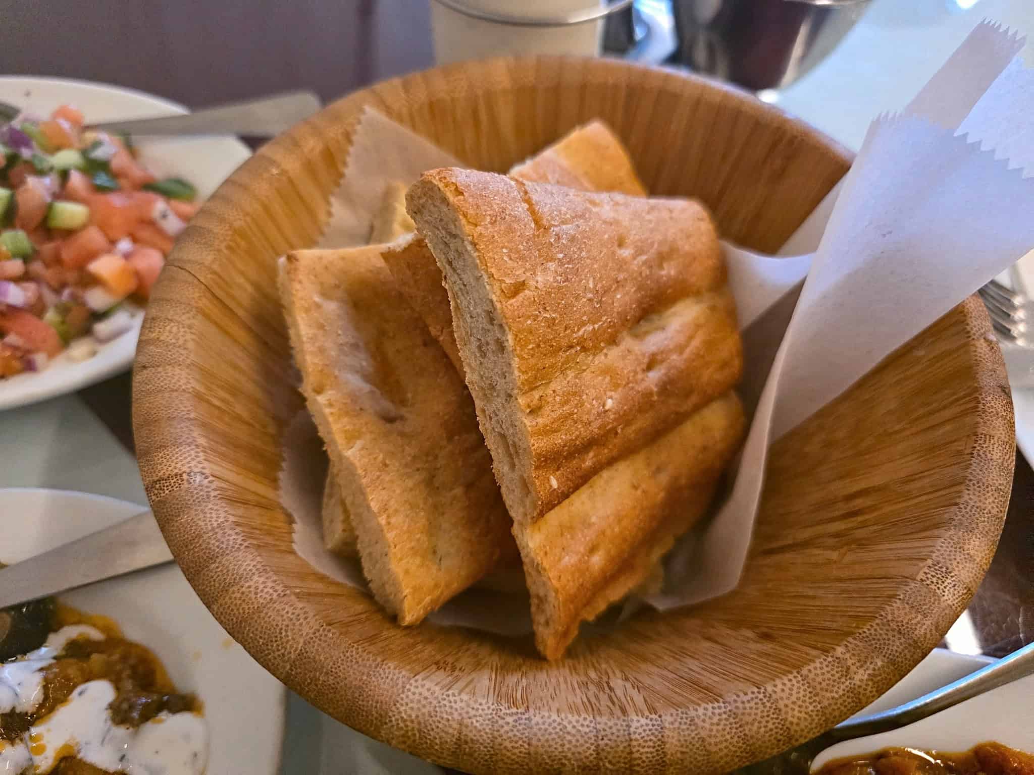 Wooden bowl filled with thick sliced warm Afghan naan bread with a golden crust