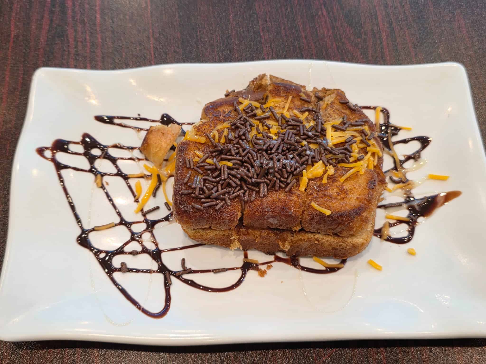 Square plate of Roti Bakar toasted bread topped with chocolate drizzle, chocolate sprinkles, and shredded cheese