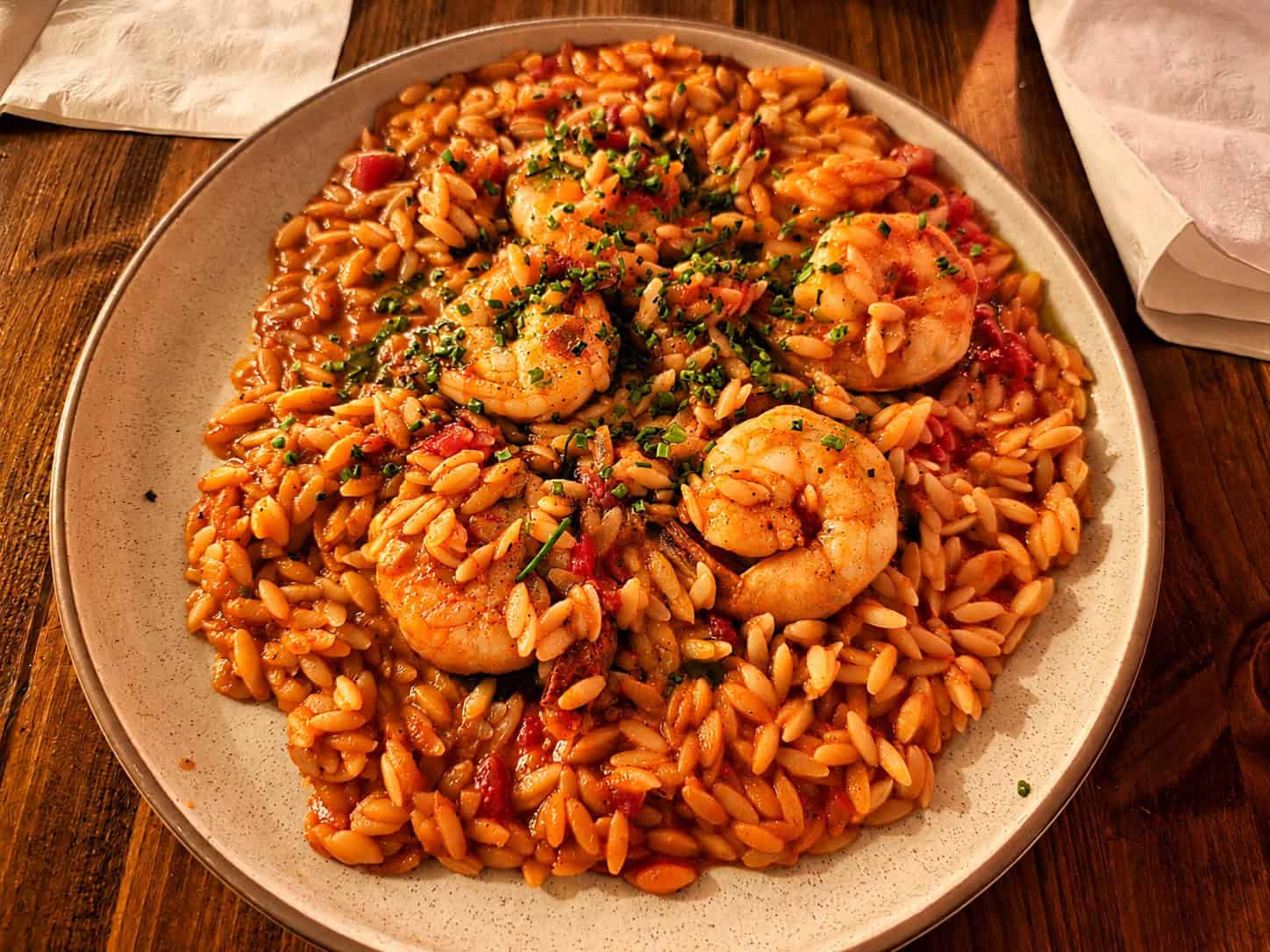 Platter of Shrimp Youvetsi featuring seared shrimp over tomato-sauced orzo pasta garnished with herbs
