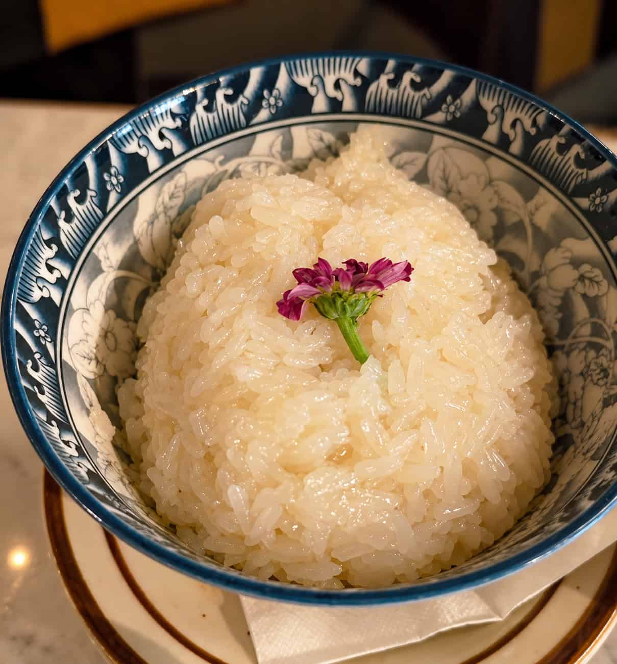 Bowl of sweet coconut sticky rice garnished with a purple flower at SaRanRom Thai