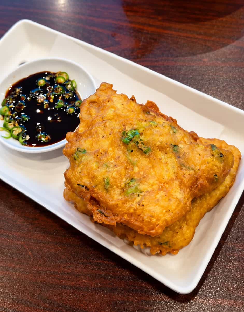 Plate of Tempeh Mendoan fried battered tempeh cakes served with dark chili soy dipping sauce