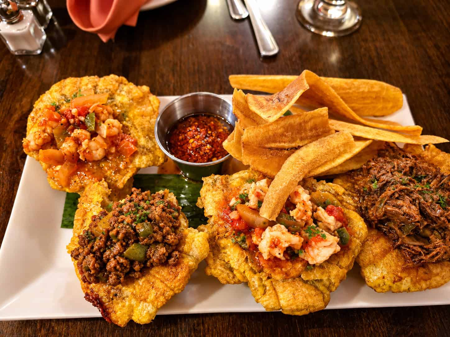 Tostones Rellenos platter featuring four fried green plantain cups topped with beef, chicken, shrimp, and picadillo alongside plantain chips and dipping sauce