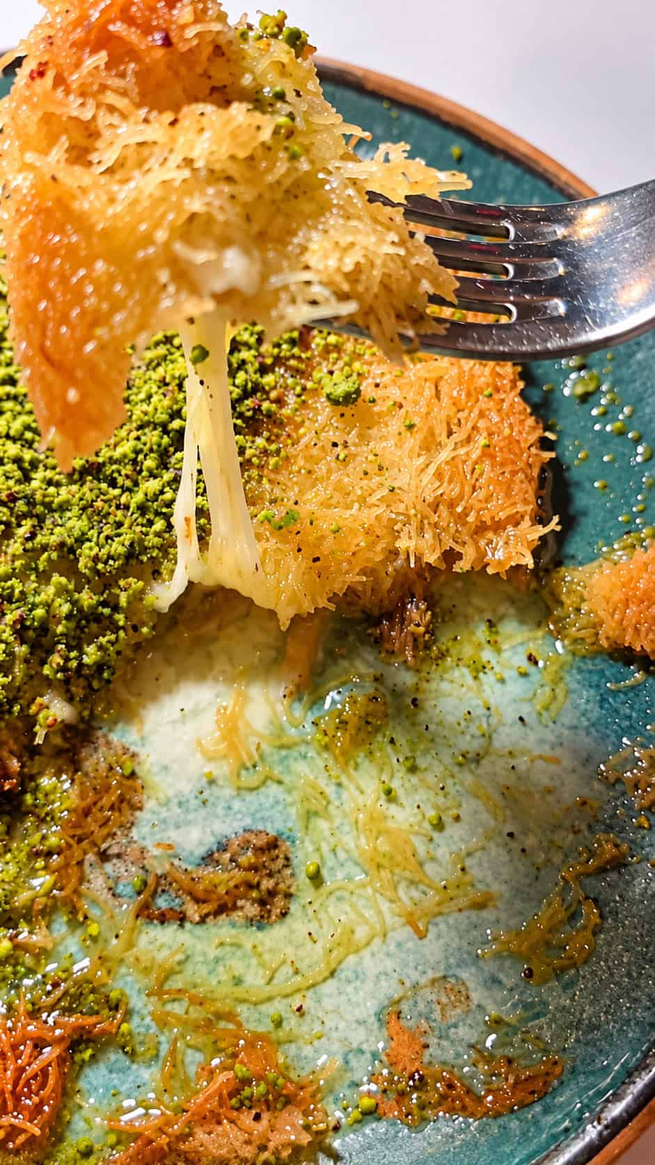 Fork lifting a piece of Turkish Kunefe showing melted cheese stretching between crispy golden pastry layers