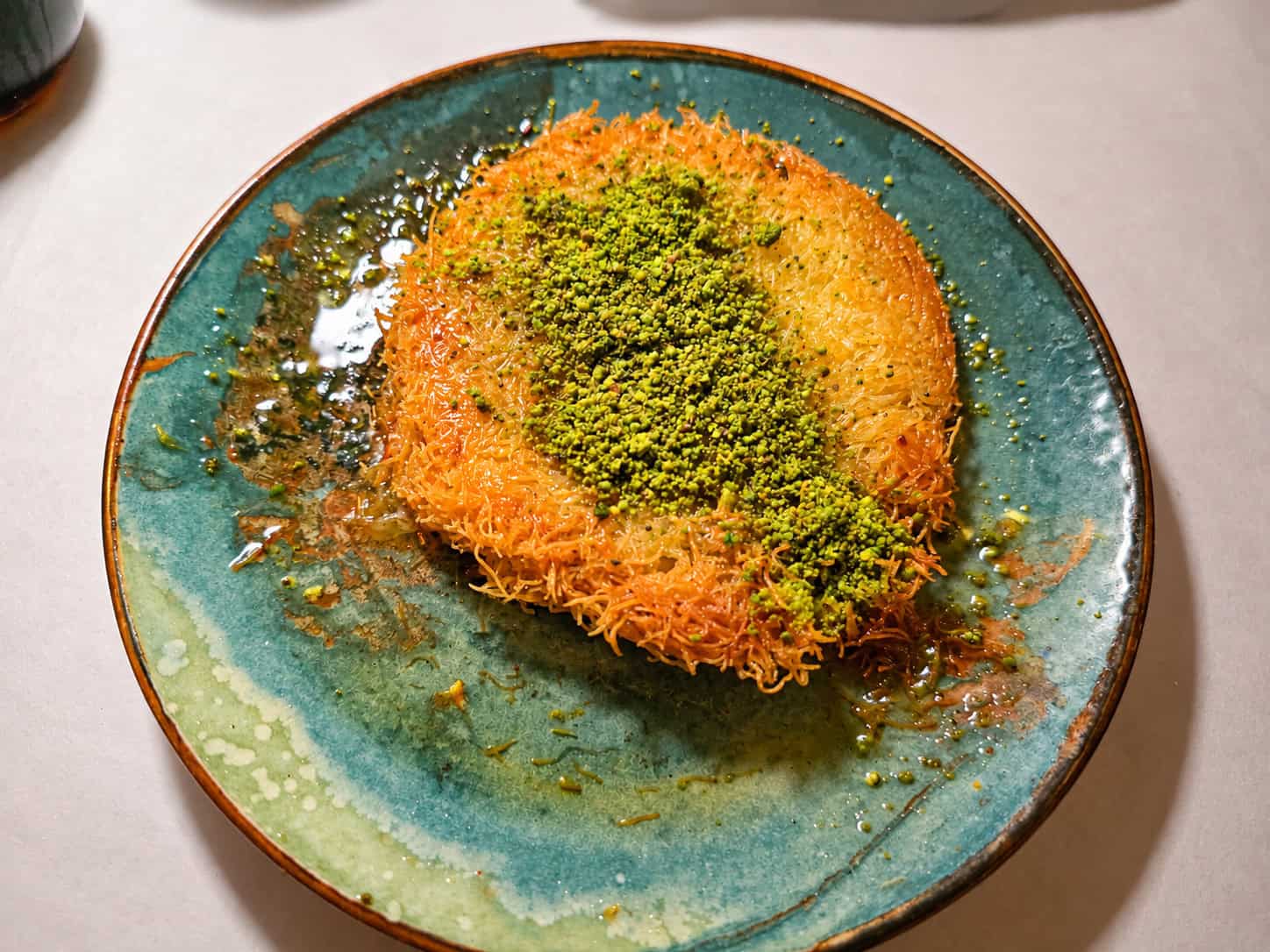 Golden shredded pastry Turkish Kunefe topped with crushed green pistachios served on a turquoise plate